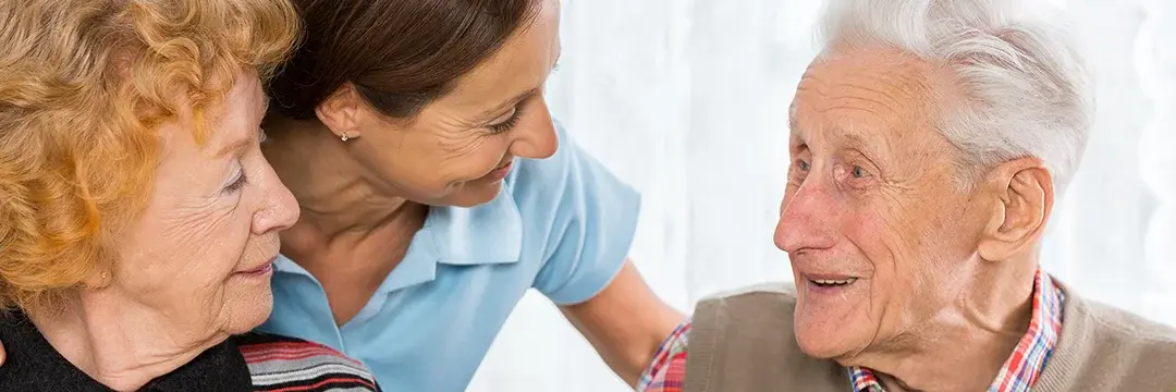 Pflegekraft unterhält sich freudig mit zwei älteren Personen