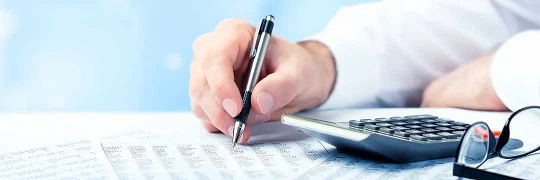 Mann mit Stift und Taschenrechner auf dem Schreibtisch (Symbolbild)