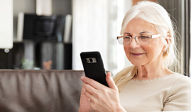 Das Bild zeigt eine ältere Frau, die auf einem Smartphone tippt. Was sie tippt, ist für den Betrachter nicht erkennbar. 