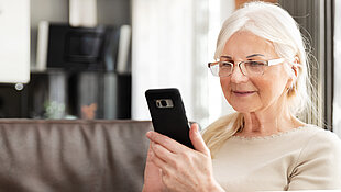 Das Bild zeigt eine ältere Frau, die auf einem Smartphone tippt. Was sie tippt, ist für den Betrachter nicht erkennbar. 