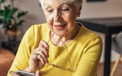 Eine ältere Frau hält eine Dose mit Nahrungsergänzungsmitteln in der Hand und informiert sich auf dem Smartphone über weitere Produkte.