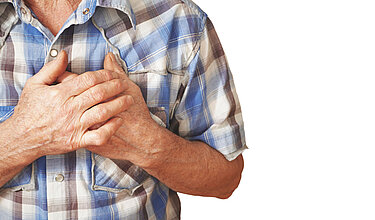 Älterer Mann fasst sich mit beiden Händen an die Brust: Symbolbild für koronare Herzkrankheit (KHK)