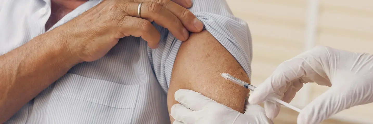 Grippeschutzimpfung Hand sticht mit einer Spritze in den Oberarm einer Person