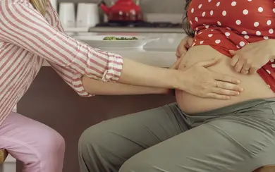 Das Bild zeigt eine Hebamme, die den Bauch einer Schwangeren untersucht.