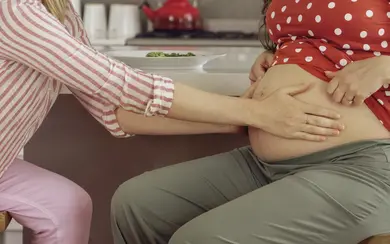 Das Bild zeigt eine Hebamme, die den Bauch einer Schwangeren untersucht.