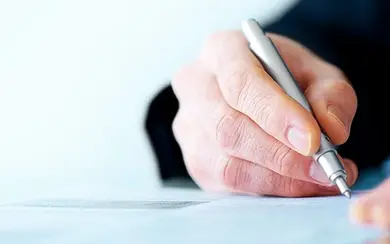 Mann hält einen Stift und unterschreibt ein Blatt Papier