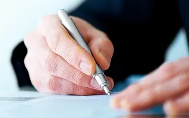 Mann hält einen Stift und unterschreibt ein Blatt Papier
