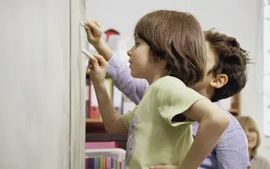 Zwei Kinder schreiben etwas an die Tafel im Klassenzimmer ihrer Schule.