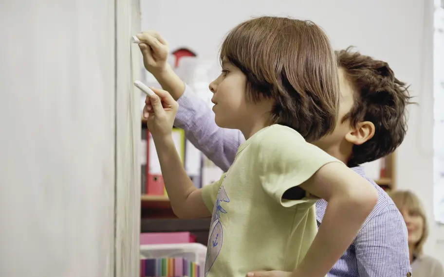 Zwei Kinder schreiben etwas an die Tafel im Klassenzimmer ihrer Schule.