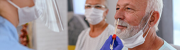 Nasenabstrich: Pflegerin steckt ein Stäbchen für einen Corona Test in die Nase eines älteren Mannes