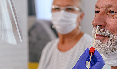 Nasenabstrich: Pflegerin steckt ein Stäbchen für einen Corona Test in die Nase eines älteren Mannes