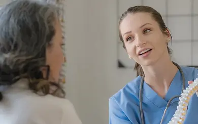 Junge Ärztin erklärt einer Patientin anschaulich ein Wirbelsäulenmodell und erläutert dabei freundlich die Zusammenhänge.