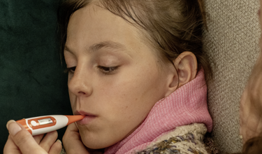 Krankes Kind mit Fieberthermometer im Mund. Bild zur Illustrierung des Mangels an Fiebersaft im Winter 2023.