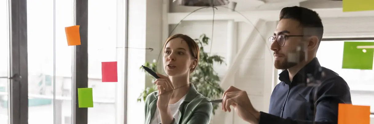 Zwei junge Personen diskutieren an einer Glaswand über Workflows diskutiert oder Arbeitsprojektprozesse: Symbolbild für Innovation und agiles Arbeiten Zwei junge Personen diskutieren an einer Glaswand über Workflows diskutiert oder Arbeitsprojektprozesse: Symbolbild für Innovation und agiles Arbeiten