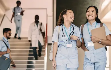 Junge Pflegerinnen laufen lächelnd durch ein Gebäude