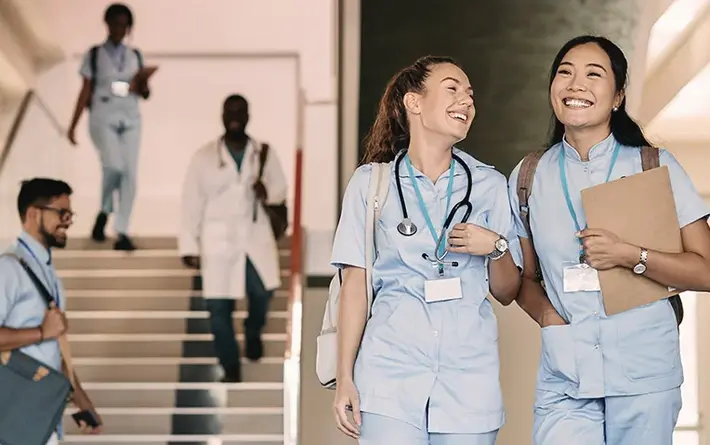 Junge Pflegerinnen laufen lächelnd durch ein Gebäude