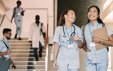 Junge Pflegerinnen laufen lächelnd durch ein Gebäude