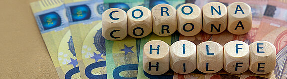 Buchstabenbausteine, die auf Geldscheinen liegen, die das Wort Coronahilfe ergeben