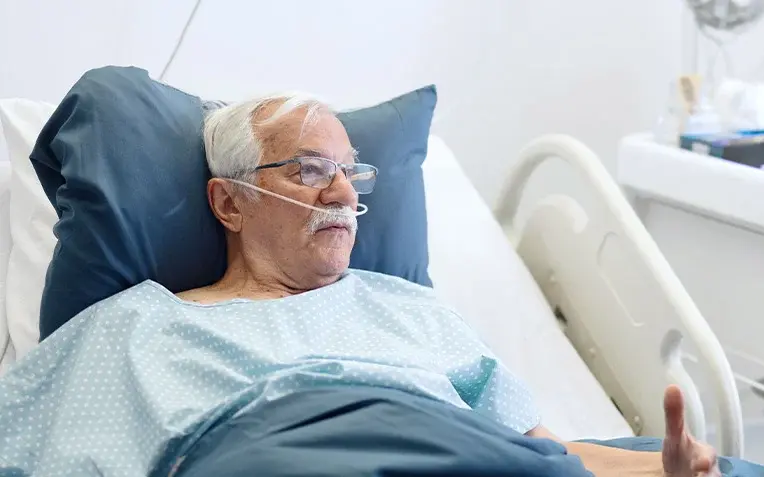 Ärztin spricht im Krankenzimmer mit einem älteren Patienten im Krankenhausbett.