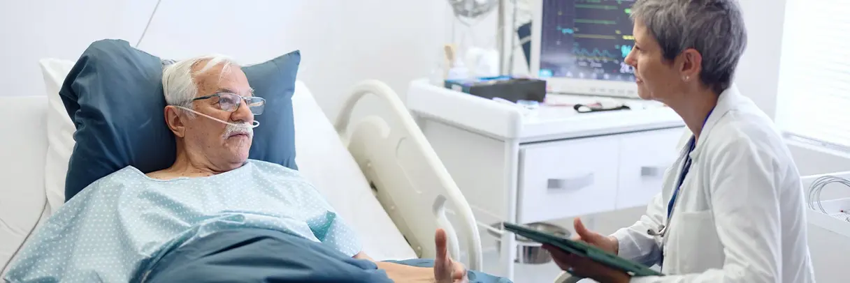 Ärztin spricht mit älterem Patienten Ärztin spricht im Krankenzimmer mit einem älteren Patienten im Krankenhausbett.