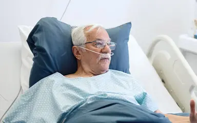 Ärztin spricht im Krankenzimmer mit einem älteren Patienten im Krankenhausbett.