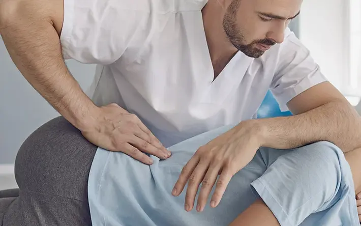 Das Bild zeigt einen Physiotherapeuten, der eine Patientin mit Rückenschmerzen behandelt. 