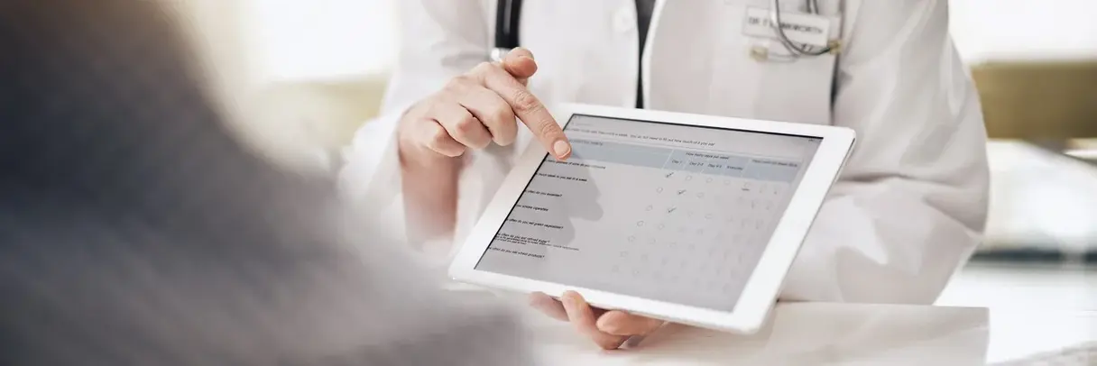 Fragebogen zur Krankenhauszufriedenheit (Symbolbild) Arzt zeigt auf Tablet mit Fragebogen zur Krankenhauszufriedenheit, Patient im Vordergrund unscharf