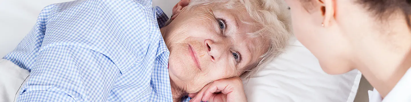Ältere Frau, die im Bett liegt, schaut freundlich eine Krankenschwester an
