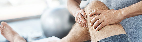 Therapeut massiert das Kniegelenk eines Patienten