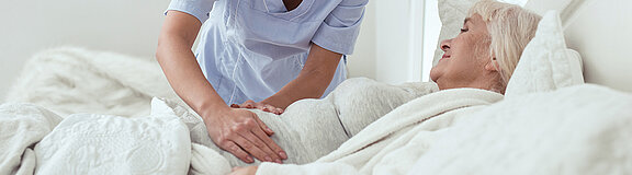 Weibliche Pflegekraft tastet den Bauch einer älteren Frau die im Bett liegt
