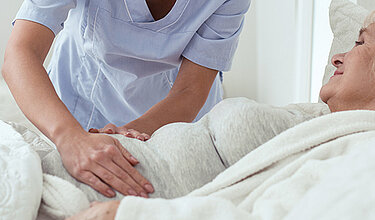 Weibliche Pflegekraft tastet den Bauch einer älteren Frau die im Bett liegt