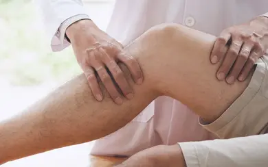 Arzt untersucht das Knie eines Patienten, Fokus auf das Bein und die Hände des Arztes