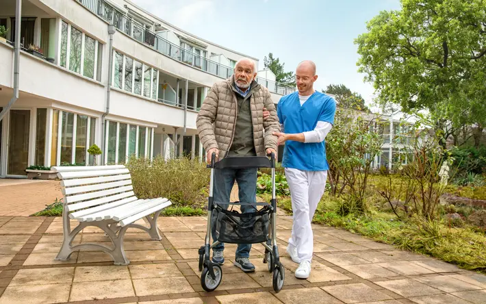 Älterer Mann mit Rollator gestützt von einem Altenpfleger