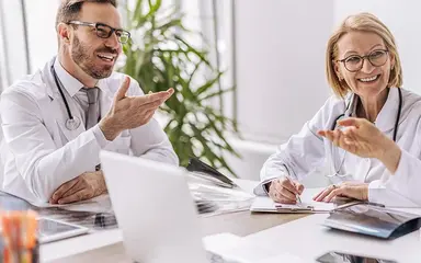 Drei Ärzte in weißen Kitteln sitzen an einem Tisch und diskutieren freundlich miteinander in einem hellen Büro