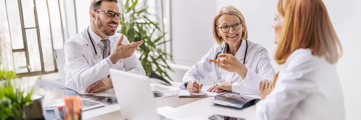 Ärztinnen und Ärzte arbeiten zusammen Drei Ärzte in weißen Kitteln sitzen an einem Tisch und diskutieren freundlich miteinander in einem hellen Büro