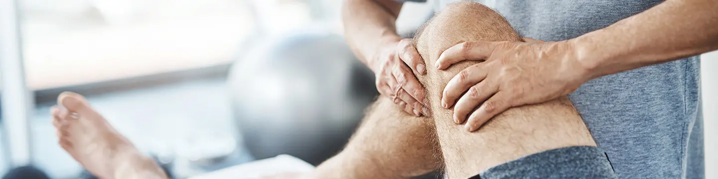 Therapeut massiert das Kniegelenk eines Patienten