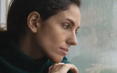 Symbolbild Depression zeigt Frau, die durch eine Scheibe in den Regen schaut