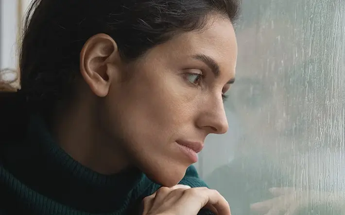 Symbolbild Depression zeigt Frau, die durch eine Scheibe in den Regen schaut