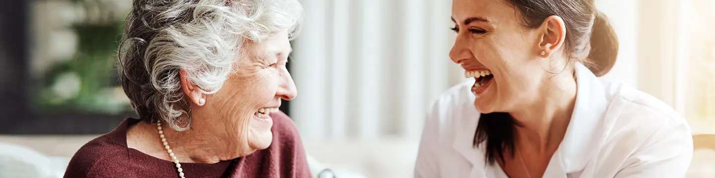 Pflegeheimbewohnerin lacht mit junger Pflegekraft