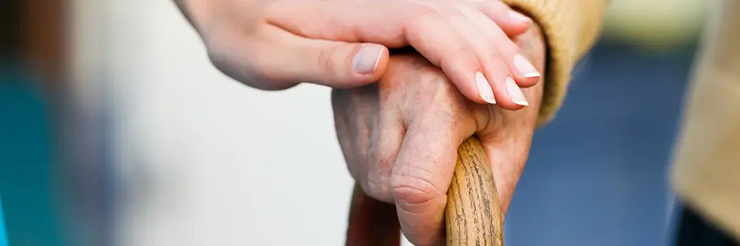 Frau legt ihre Hand auf die eines Senionren der seine Gehilfe hält Frau legt ihre Hand auf die eines Senionren der seine Gehilfe hält Frau berührt Senionrenhand auf einer Gehilfe