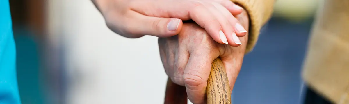 Frau legt ihre Hand auf die eines Senionren der seine Gehilfe hält Frau berührt Senionrenhand auf einer Gehilfe 