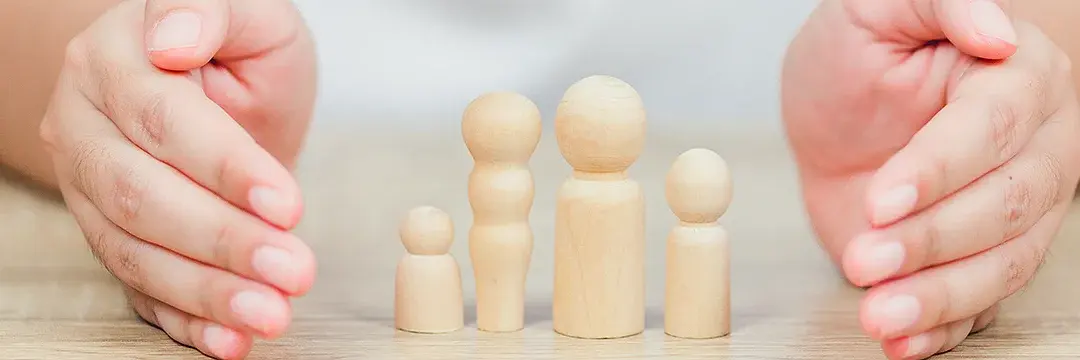 Zwei Hände schützen mehrere Holzfiguren