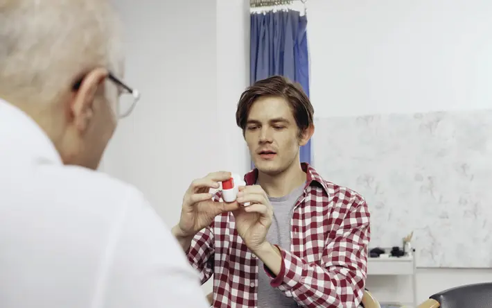 Das Bild zeigt einen Arzt und einen Patienten im Gespräch. Der Patient hält einen Inhalator zur Behandlung von Lungenerkrankungen in der Hand. 