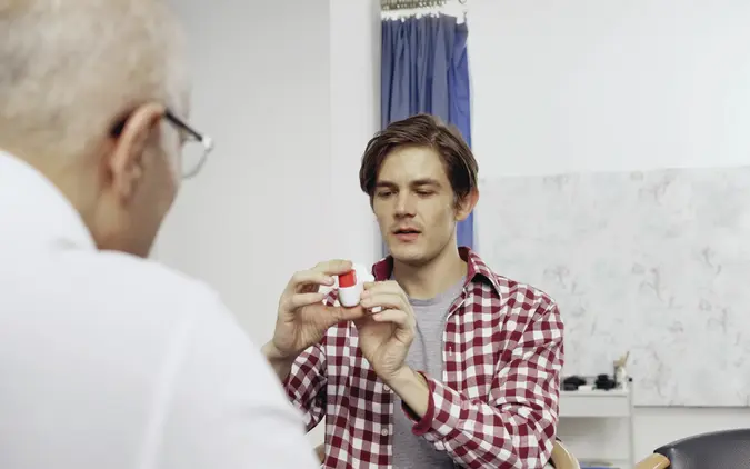 Das Bild zeigt einen Arzt und einen Patienten im Gespräch. Der Patient hält einen Inhalator zur Behandlung von Lungenerkrankungen in der Hand. 