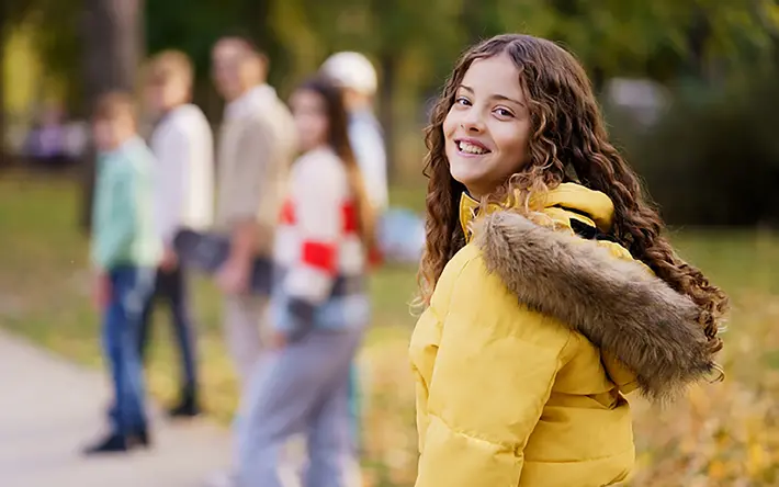 Das Bild zeigt im Vordergrund ein Mädchen im Teenager-Alter, im Hintergrund eine Gruppe von weiteren Mädchen im gleichen Alter.