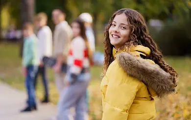 Das Bild zeigt im Vordergrund ein Mädchen im Teenager-Alter, im Hintergrund eine Gruppe von weiteren Mädchen im gleichen Alter.