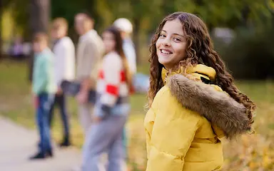 Das Bild zeigt im Vordergrund ein Mädchen im Teenager-Alter, im Hintergrund eine Gruppe von weiteren Mädchen im gleichen Alter.