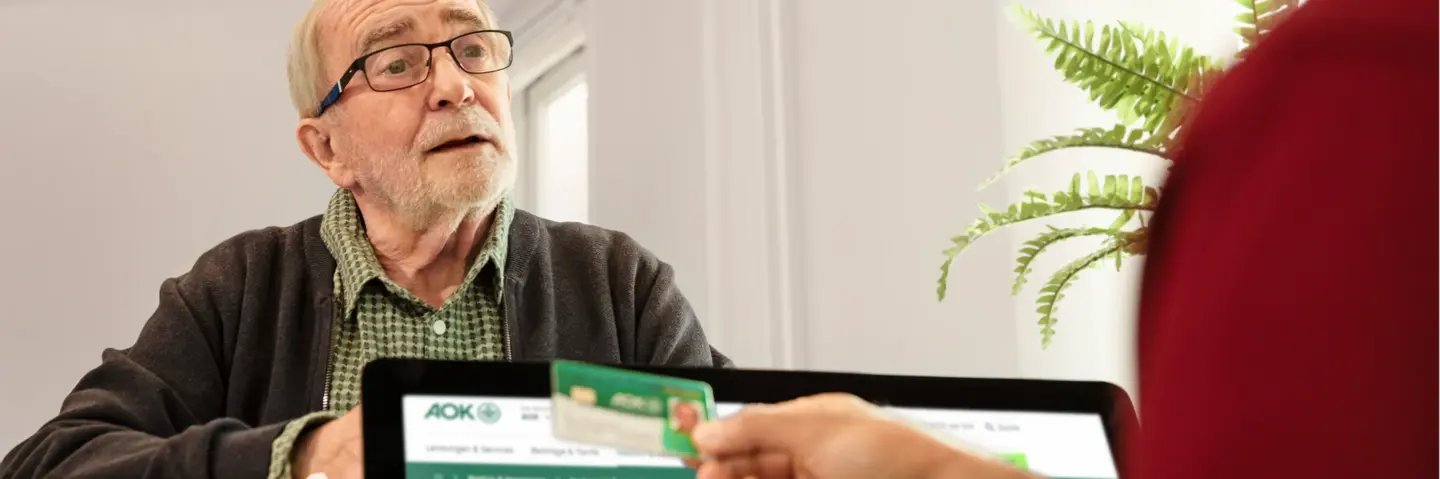 Patient meldet sich in Arztpraxis an und zeigt seine Gesundheitskarte. 