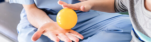 Ergotherapeut und Kind, haben in einer Hand mit einem kleinen Ball und machen Übung