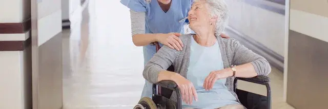 Ältere Dame, die in einem Rollstuhl sitzt, lächelt eine weibliche Pflegekraft an. Ältere Dame, die in einem Rollstuhl sitzt, lächelt eine weibliche Pflegekraft an.